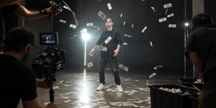 Performer stands beneath falling prop bills during a controlled music-video shoot.