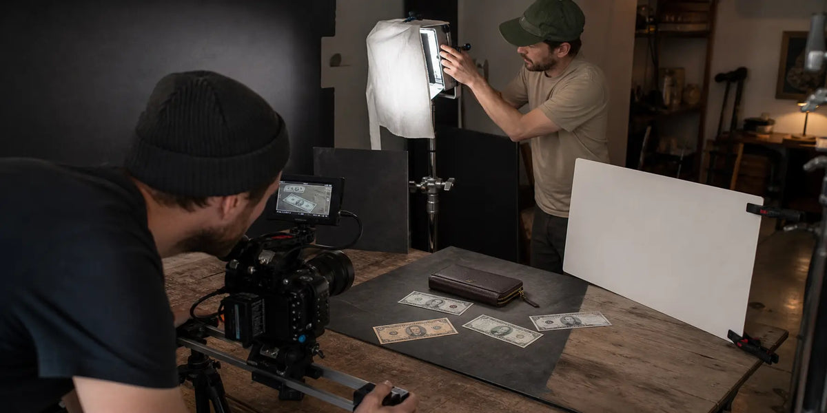 Small production crew using practical lighting and a camera slider to film a professional tabletop commercial with prop bills.