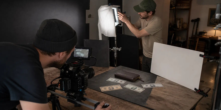 Small production crew using practical lighting and a camera slider to film a professional tabletop commercial with prop bills.
